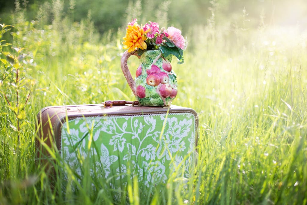 A colorful floral jug on a vintage suitcase in a sunny summer meadow.